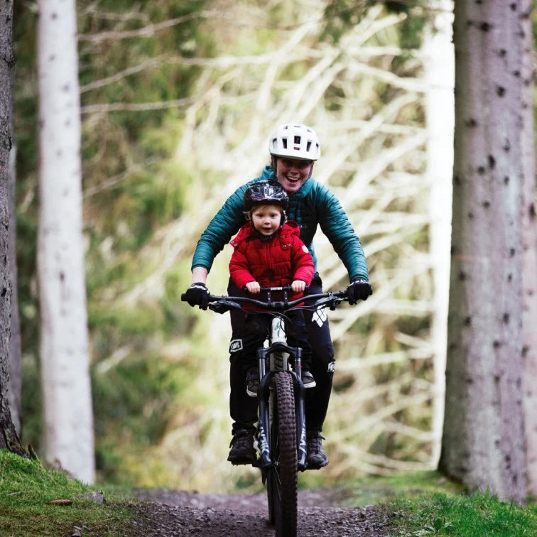 Front view of an adult and child riding together on a forest path