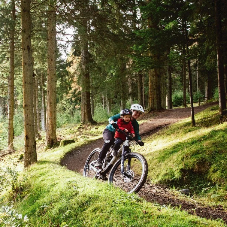 Adult and child riding a mountain bike on a forest trail
